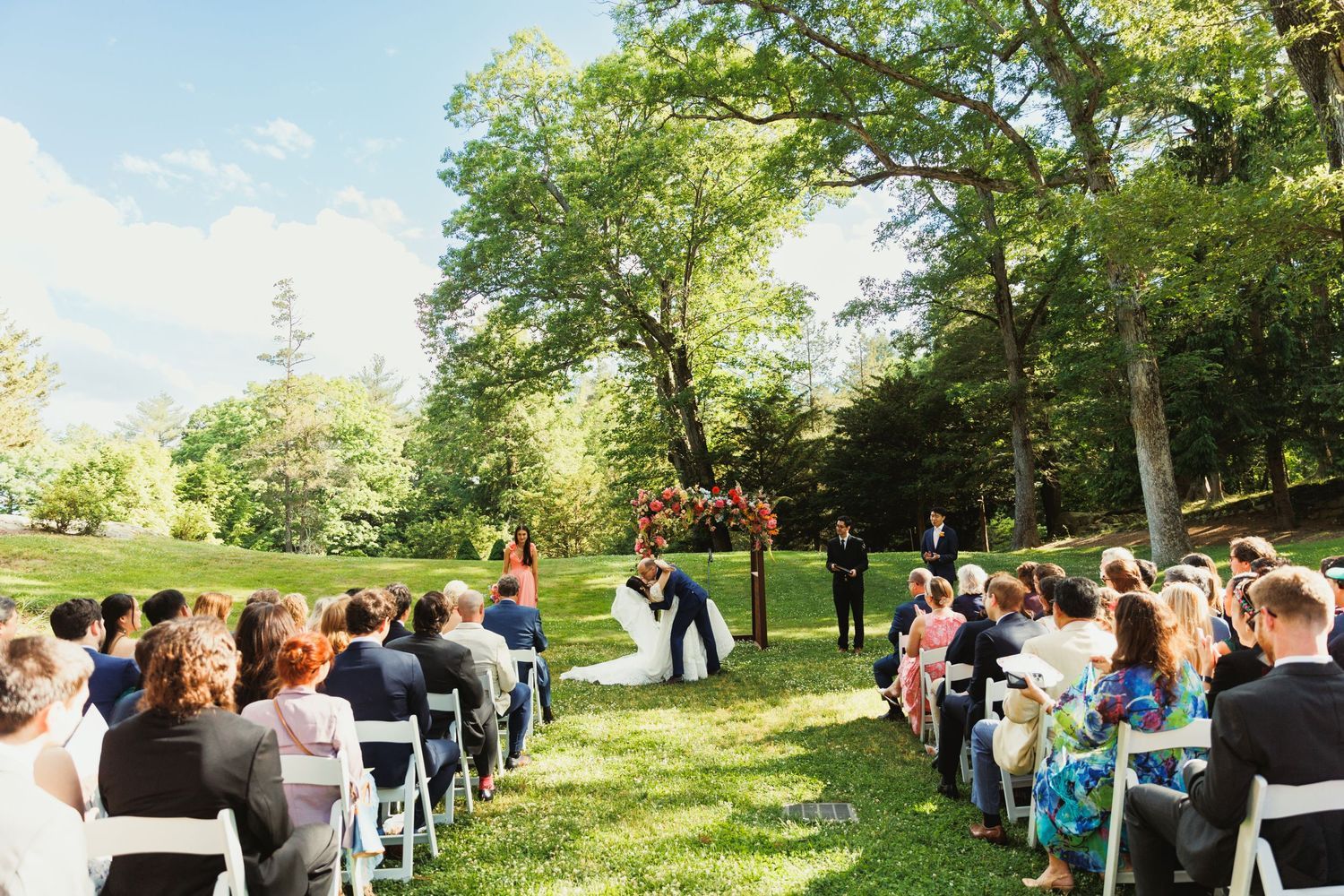 Outdoor garden ceremony under mature trees with seated guests